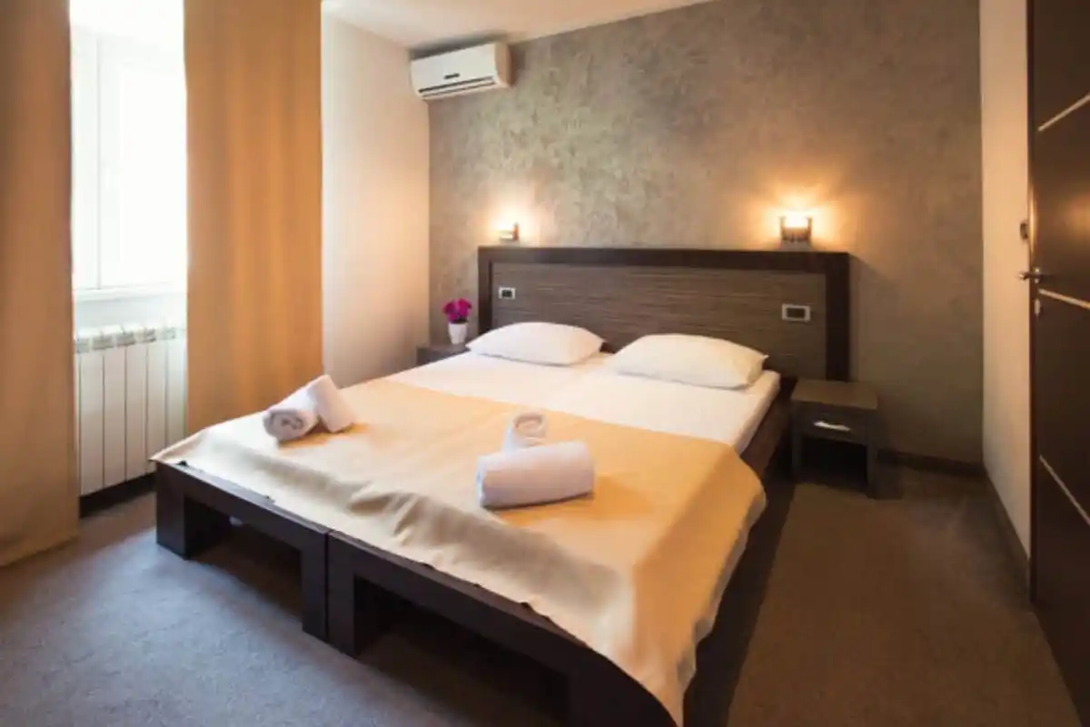 Cozy hotel room with wall-mounted air conditioner above the bed, representing the benefits of AC in hotel rooms for guest comfort and restful sleep.