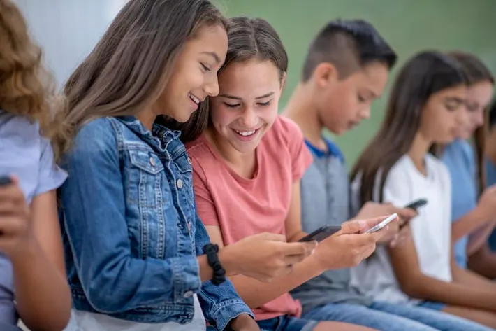 Smiling Gen Alpha teens sharing content on mobile — highlighting peer influence and the need for brand marketing to Gen Alpha in digital marketing Gold Coast campaigns.