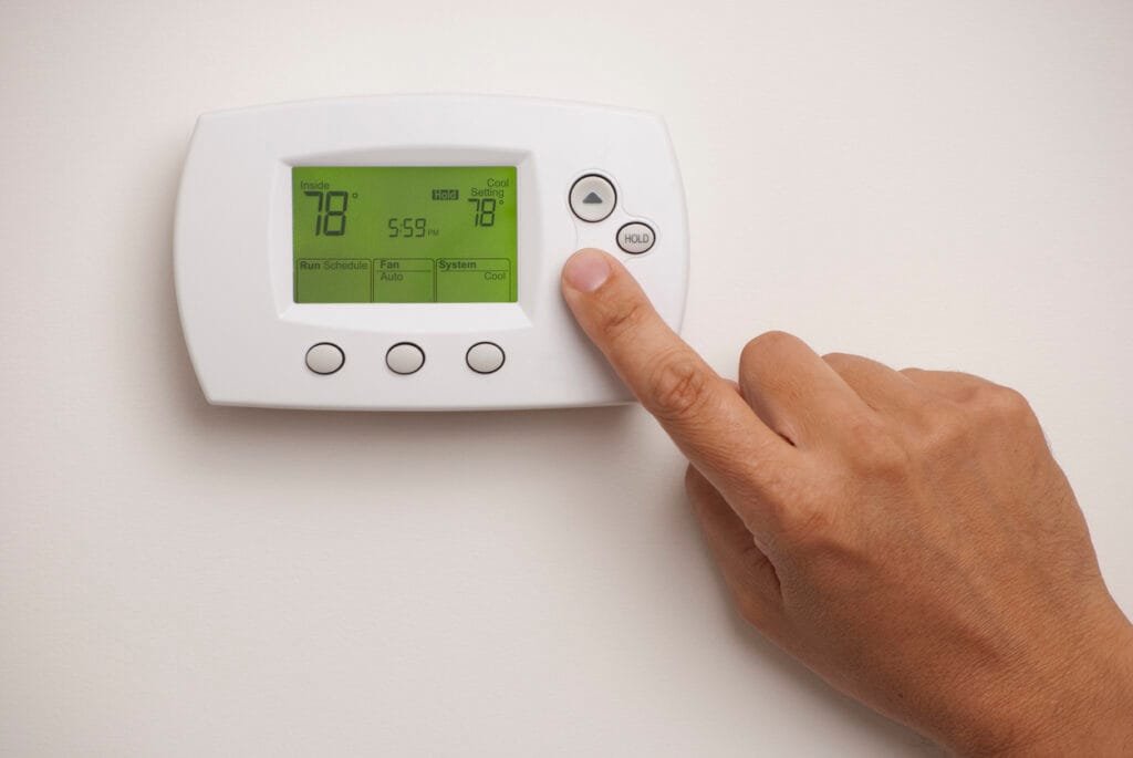 A person pressing the “up” button on a digital thermostat, possibly adjusting settings to turn off HVAC when it isn’t heating.