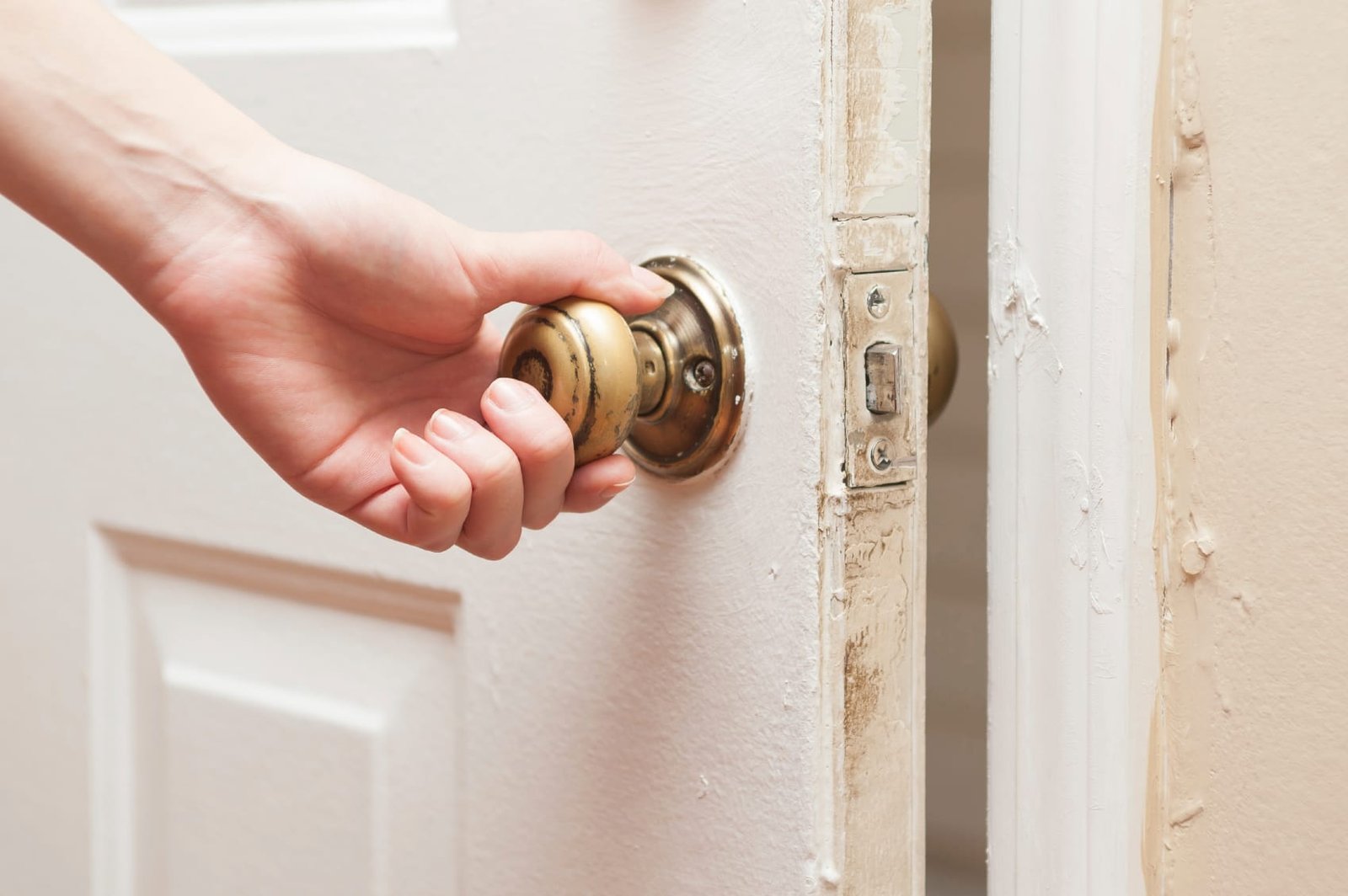 Close-up of a hand turning an old brass doorknob on a partially opened door, representing the decision to leave doors open or closed in home settings.